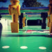 Close-up view of a Tornado Classic foosball table showing black and yellow player figures on metal rods. The green field features white markings, simulating a soccer pitch. Durable design elements indicate a tournament-grade construction.