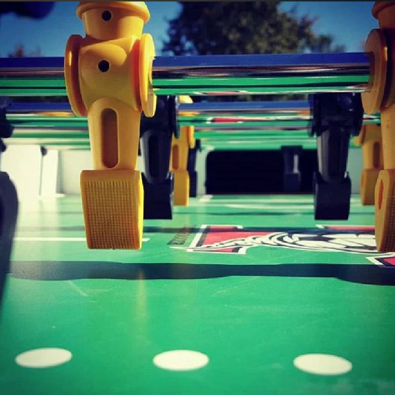 Close-up view of a Tornado Classic foosball table showing black and yellow player figures on metal rods. The green field features white markings, simulating a soccer pitch. Durable design elements indicate a tournament-grade construction.